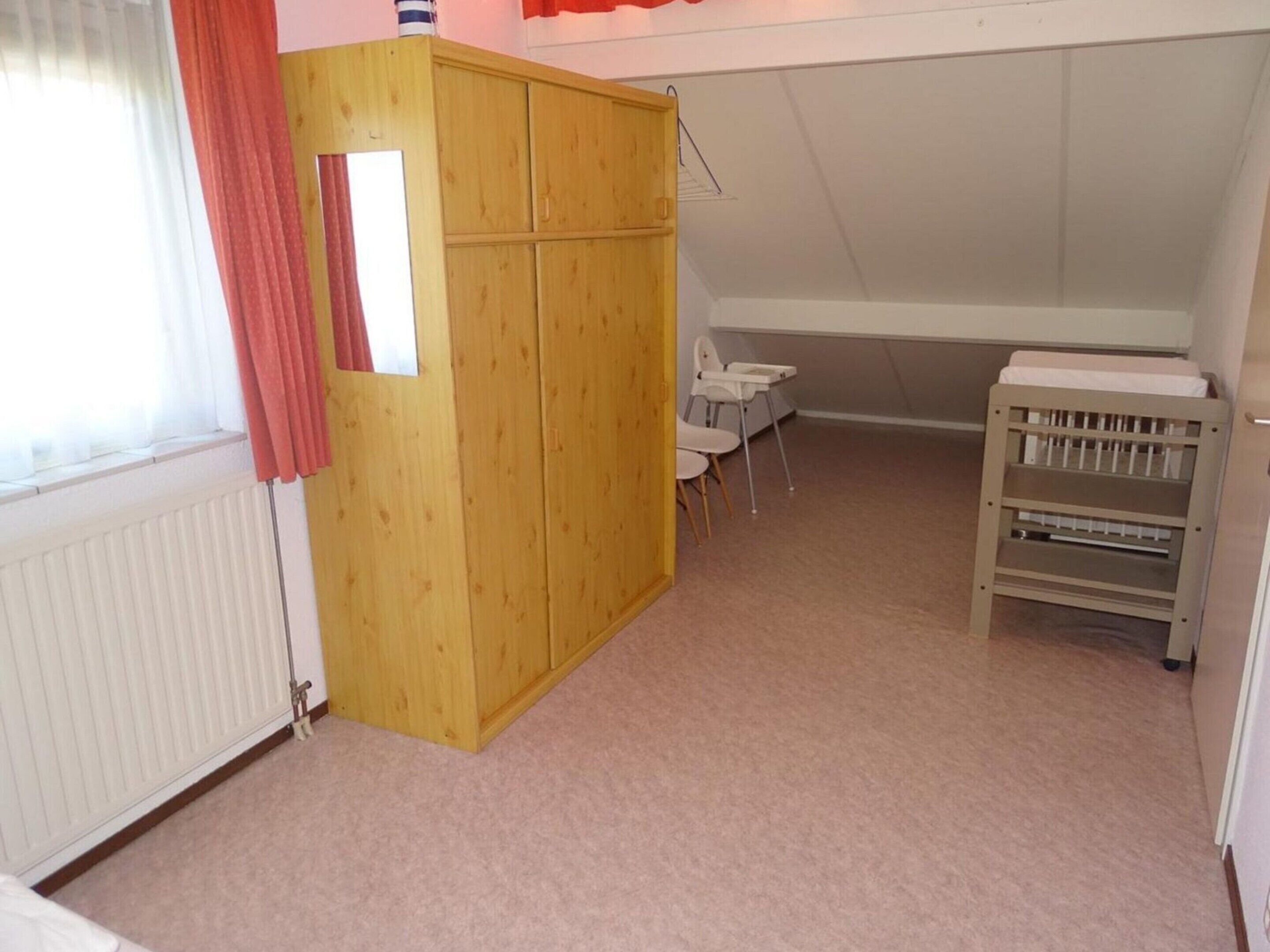 A room with a wooden wardrobe, a crib, and a small table with chairs.