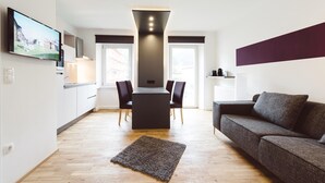 A modern living room with a sofa, a TV mounted on the wall, a dining area with chairs, and a kitchen with cabinets. - Mountain-view Styria Apartment (Eisenerz)