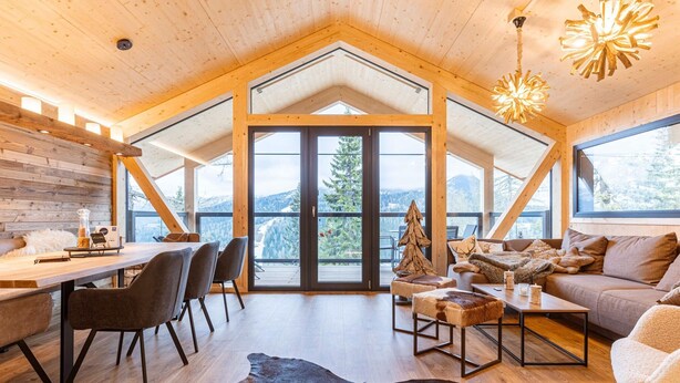A spacious room with a wooden ceiling, a large window, and a dining area with chairs and a table.