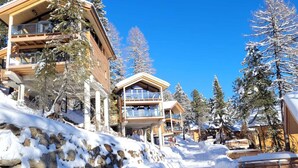A snow-covered resort with multiple-story buildings, wooden balconies, and snow-laden trees.