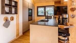 A modern kitchen with wooden cabinetry, a central island, a built-in oven, and a window overlooking greenery.