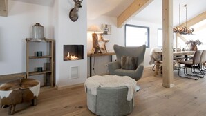 Una sala de estar acogedora con chimenea, una cabeza de venado montada en la pared, un sillón cómodo y una mesa de comedor de madera.