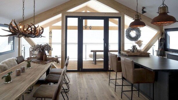 Un comedor espacioso con techo alto y vigas de madera, un ventanal y vistas al exterior.
