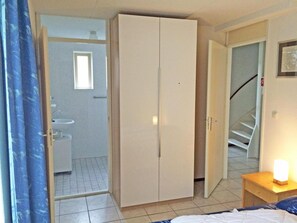 Een slaapkamer met een bed, een kledingkast, een nachtkastje met lamp en een badkamer met wastafel, plus een trap.