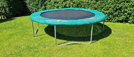 A trampoline in a grassy area with a hedge in the background.