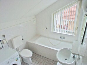 Een kleine, witte badkamer met toilet, wastafel en bad.
