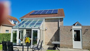 Una casa con invernadero de vidrio, un panel solar en el techo y fachada de ladrillo.