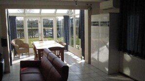Una habitación con sofá, mesa, sillas, un radiador y vistas a través de amplios ventanales.