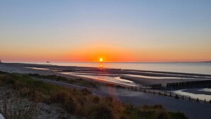 Una puesta de sol sobre una playa con un paseo marítimo y dunas.