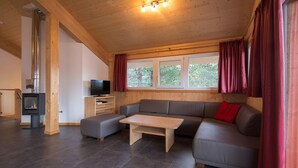A modern living room with a wooden ceiling, a fireplace, a grey sofa, a wooden coffee table, and a TV. - Lovely Chalet in Turracherhohe With Sauna (Stadl-Predlitz)