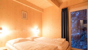 A wooden cabin room with a bed, a nightstand, a framed picture on the wall, and a window with a view of trees. - Lovely Chalet in Turracherhohe With Sauna (Stadl-Predlitz)