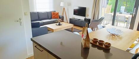 A modern living room with a sofa, a coffee table, a TV, and a dining area with a table and chairs.