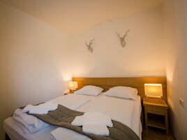 Una cama bien tendida con sábanas blancas y un plaid marrón, dos lámparas de pared y dos piezas de decoración mural con forma de astas.