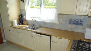 A kitchen with white cabinets, a double sink, a stove, and a window with a view of greenery. - Holiday Home Breskens Near Scenic Beaches (Breskens)