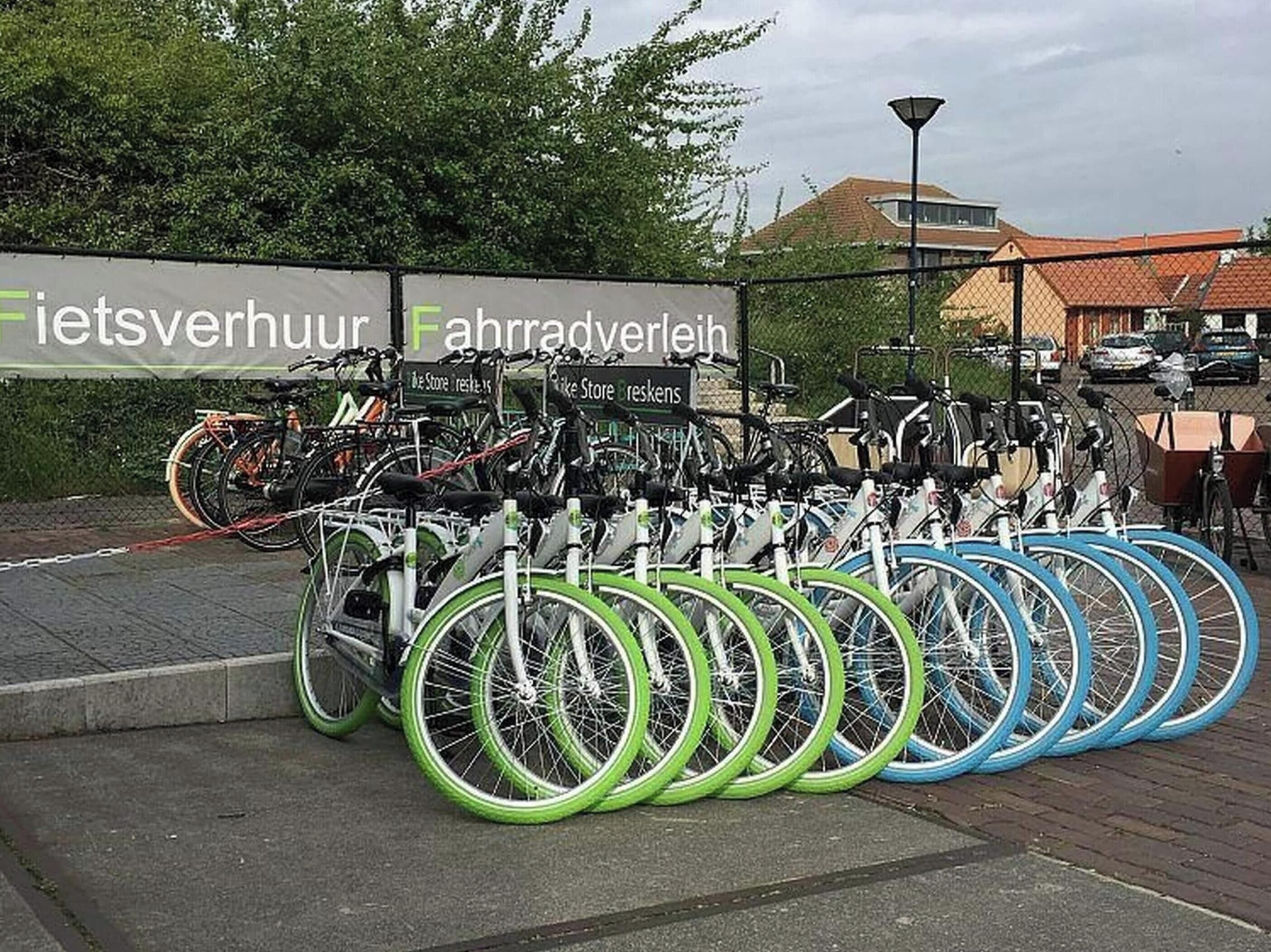 Un espace de stationnement pour vélos où sont garés plusieurs vélos, un panneau avec du texte, et un bâtiment en arrière-plan.