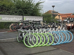 A bicycle parking area with multiple bikes, a sign with text, and a building in the background. - Holiday Home Breskens Near Scenic Beaches (Breskens)