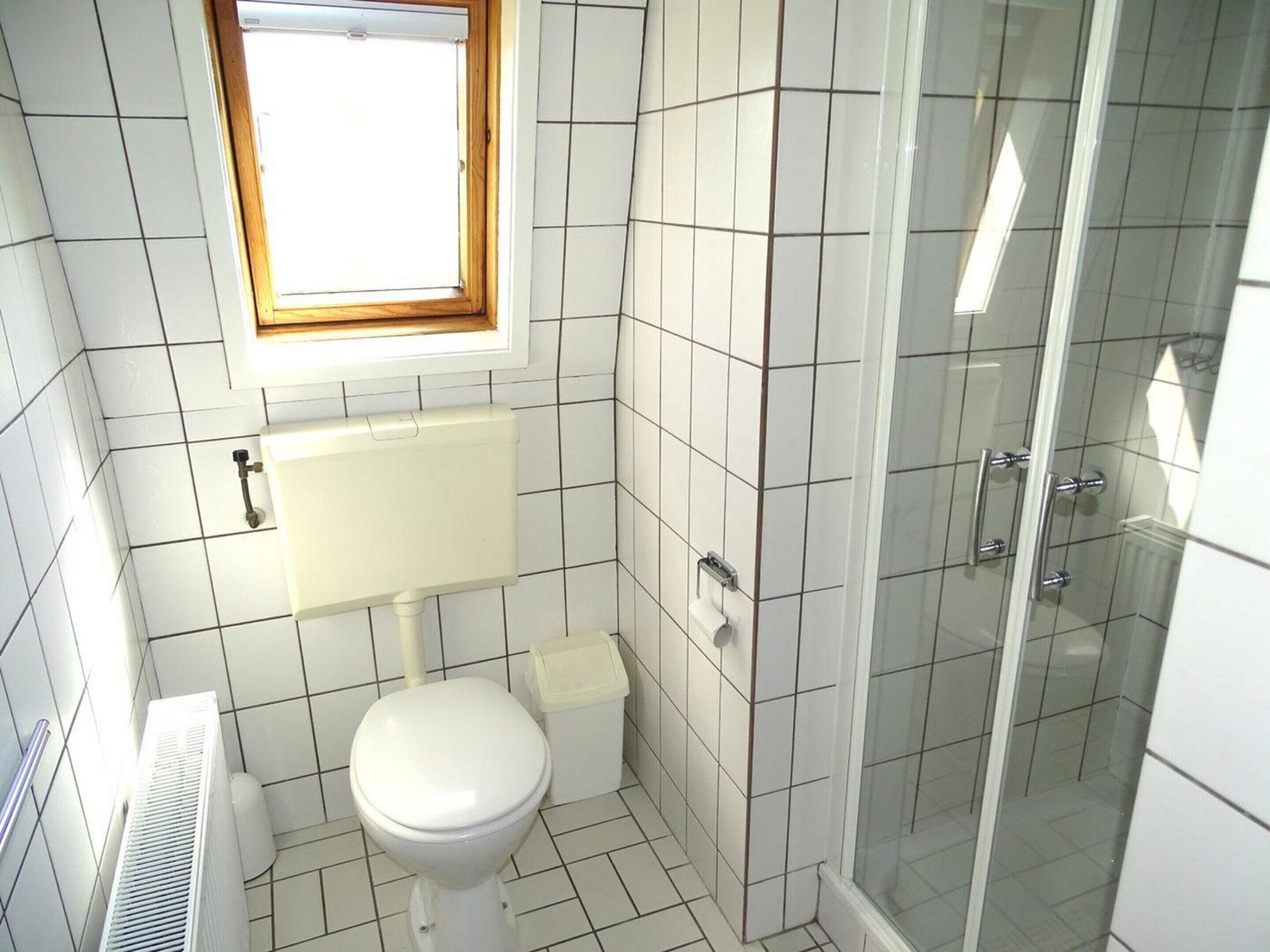 Une salle de bain équipée de toilettes, d’une fenêtre, d’une douche et d’un radiateur.