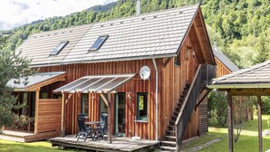 A wooden cabin with a sloped roof, a covered patio with outdoor seating, and a staircase leading to the entrance. - Cosy Apartment With Fireplace (Sankt Georgen am Kreischberg)