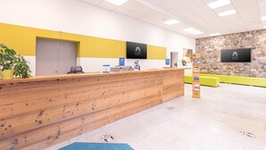 Un espace d’accueil doté d’un comptoir de réception en bois, d’un mur en pierre et d’une décoration aux couleurs jaune et blanche.