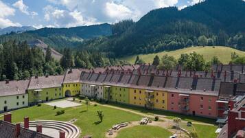 A row of multi-story buildings with a courtyard in the center, surrounded by greenery and mountains.