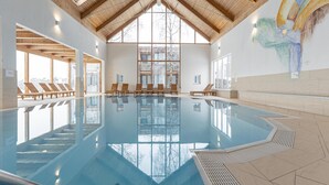Une piscine intérieure dotée de poutres en bois, de parois en verre transparent et de chaises longues.