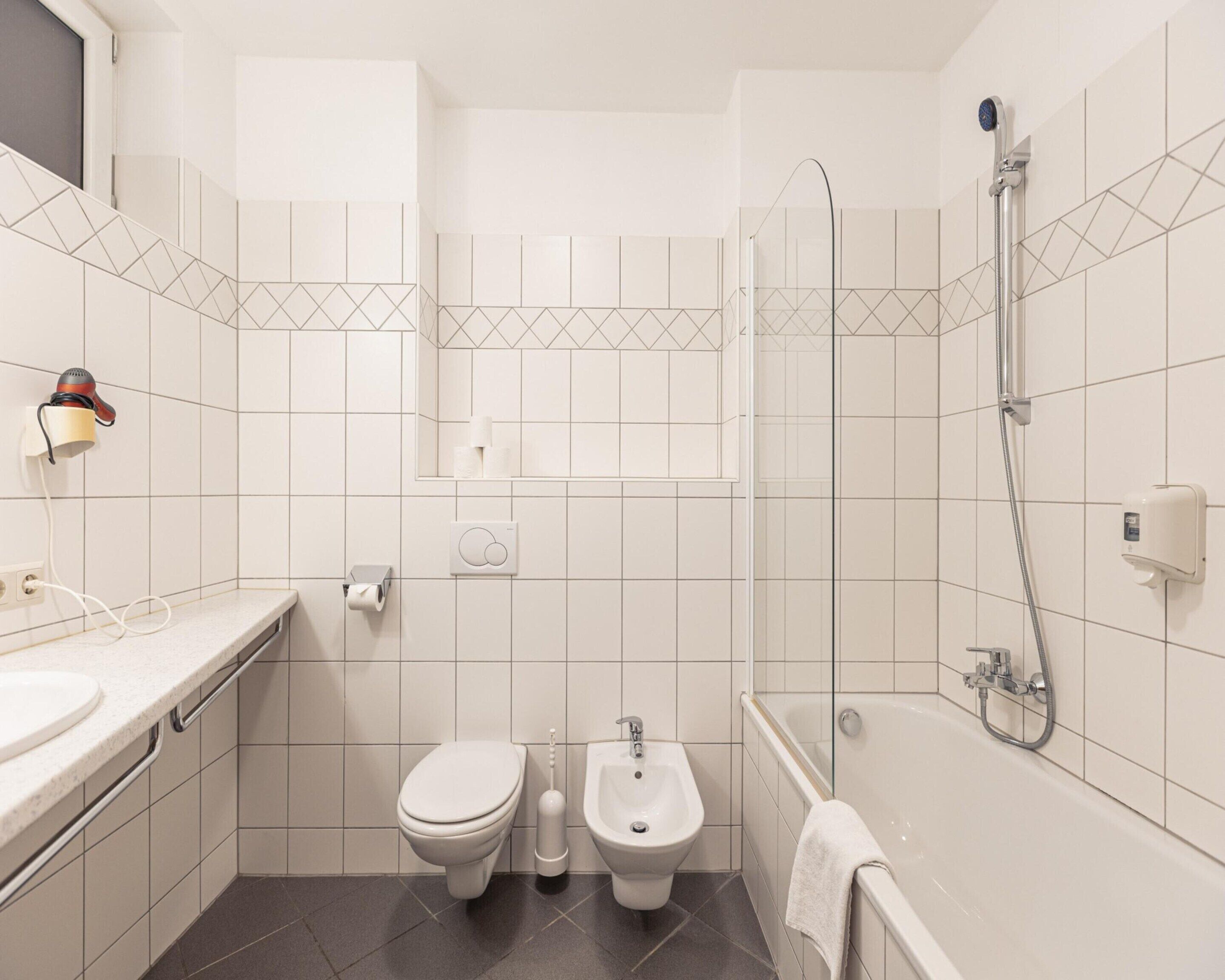 A modern bathroom with a toilet, bidet, sink, and bathtub.