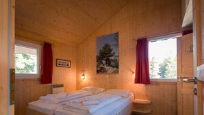 Ein Schlafzimmer in einer Holzhütte mit einem Bett, einem Fenster, einem Gemälde und einer Tür.