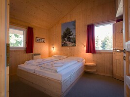 Un dormitorio de cabaña de madera con una cama, un ventanal, un cuadro y una puerta.
