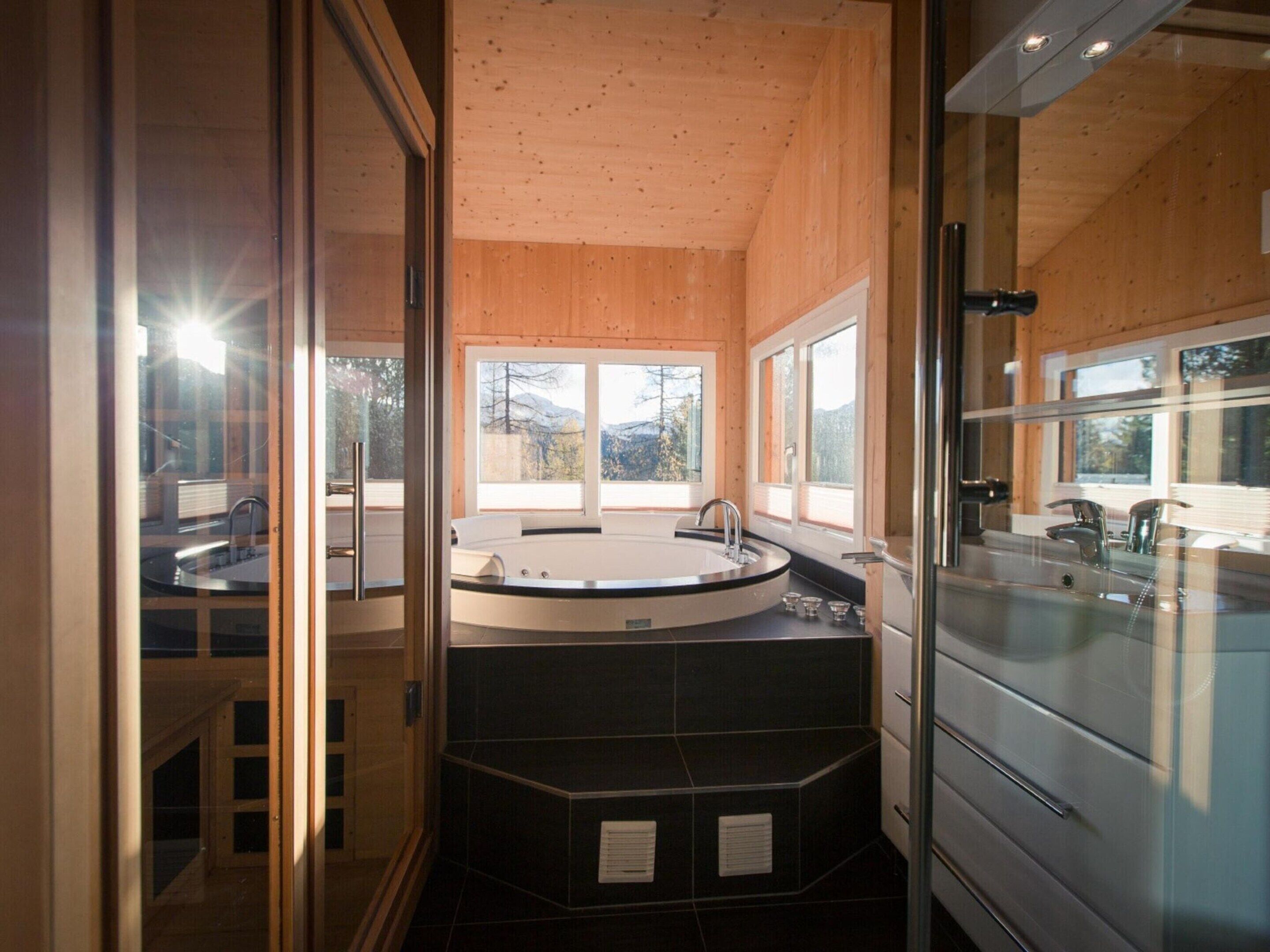 A modern bathroom with a large bathtub, a separate shower area, and a glass-enclosed sink.