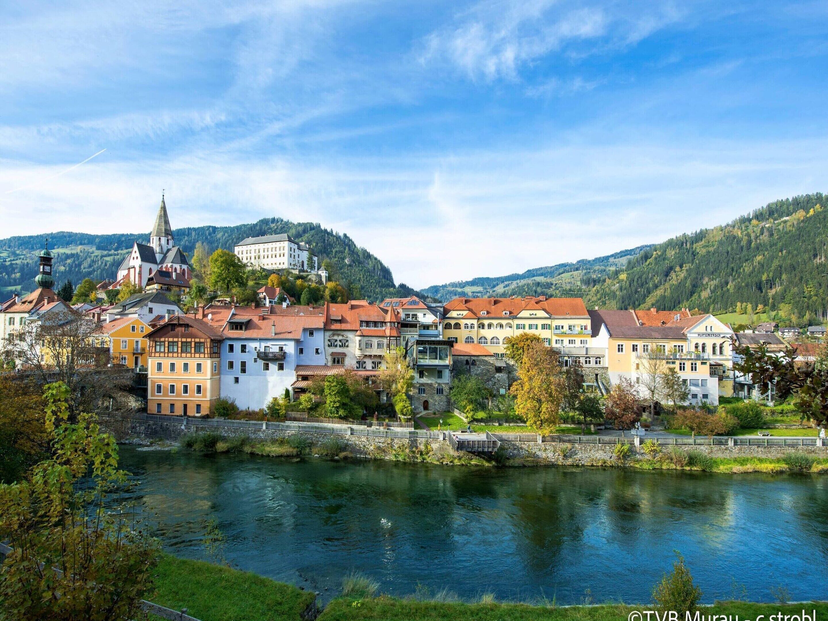 A riverside town with historic buildings, a prominent church, and a castle on a hill.