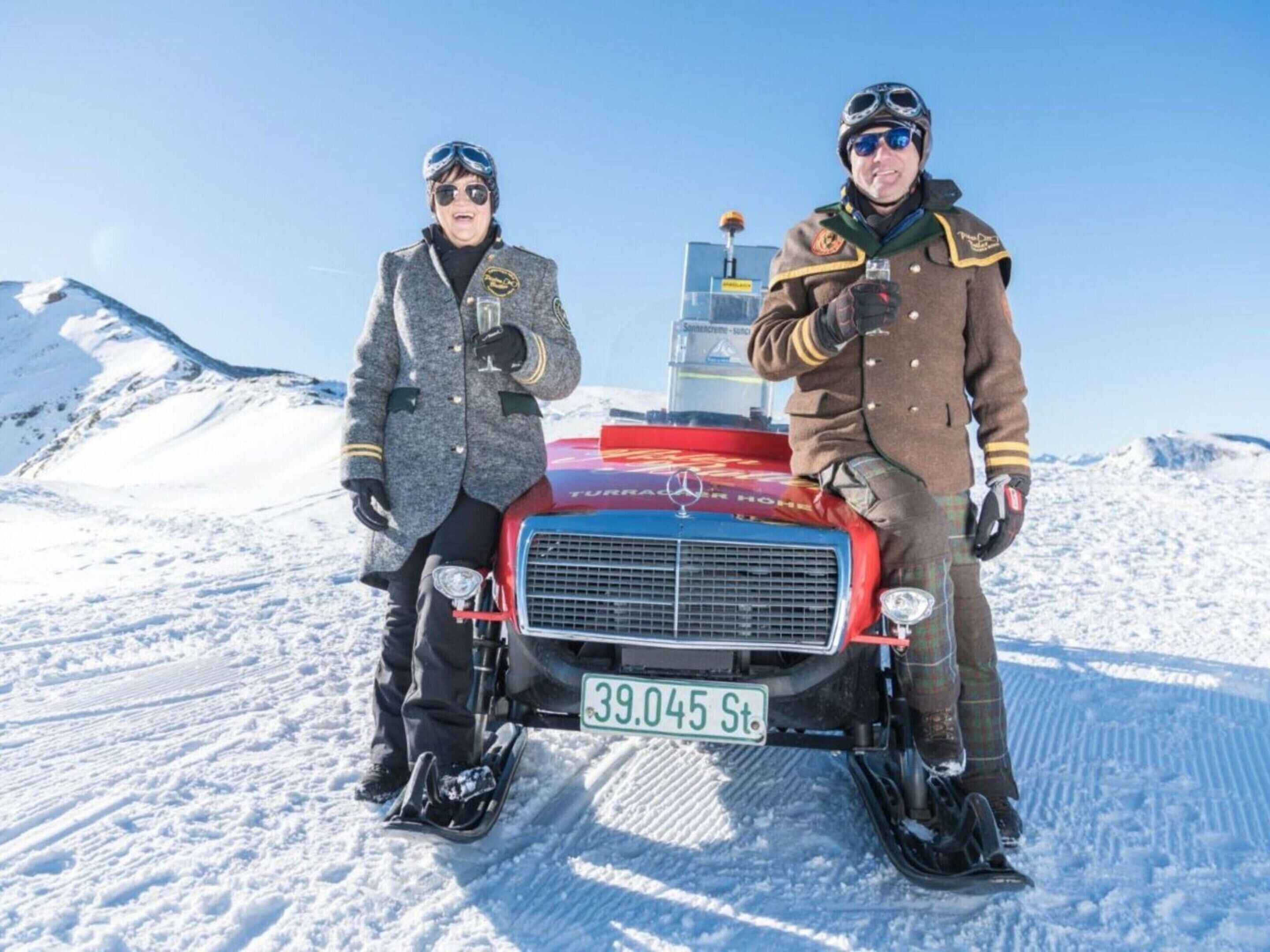 Two individuals in winter clothing standing beside a snowmobile with a license plate.