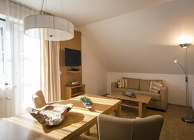 A modern living room with a wooden dining table, a sofa, a TV mounted on the wall, and a floor lamp.