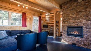 A cozy living room with a stone fireplace, a sofa, and a television. - Cozy Chalet With hot tub (Stadl-Predlitz)