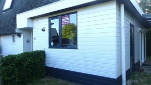 Un bâtiment blanc avec un toit noir, une fenêtre sur laquelle est apposée une enseigne, et un petit arbuste devant.