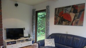 Un salon avec une télévision, un canapé, une petite table sur laquelle est posée une bougie, et un tableau accroché au mur.