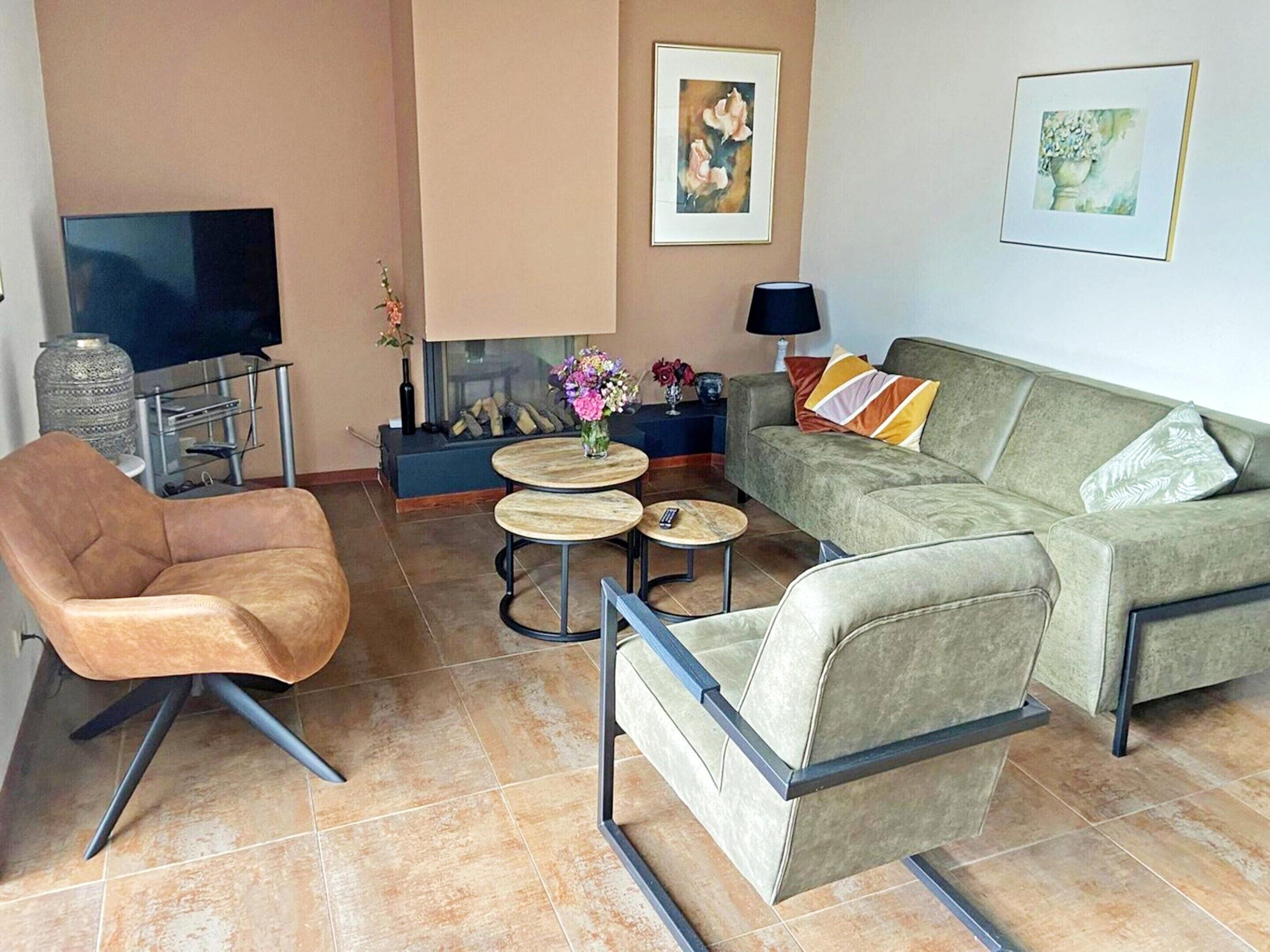 A living room with a sofa, armchair, TV, fireplace, and artwork.