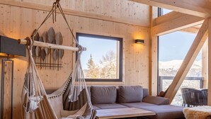 A cozy room with a hammock, a sofa, and a large window offering a view of snow-covered mountains.