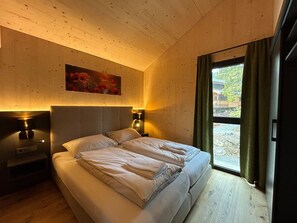A bedroom with a wooden ceiling, a bed with white linens, two bedside lamps, and a window with curtains. - Chalet With Sauna on Balcony (Stadl-Predlitz)