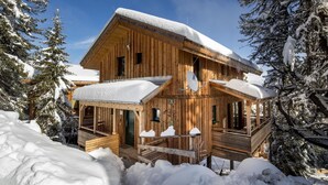Eine Holzhütte mit Balkon und überdachter Veranda, umgeben von Schnee und Bäumen.