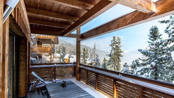 Eine Holzterrasse mit Blick auf schneebedeckte Bäume und Berge.