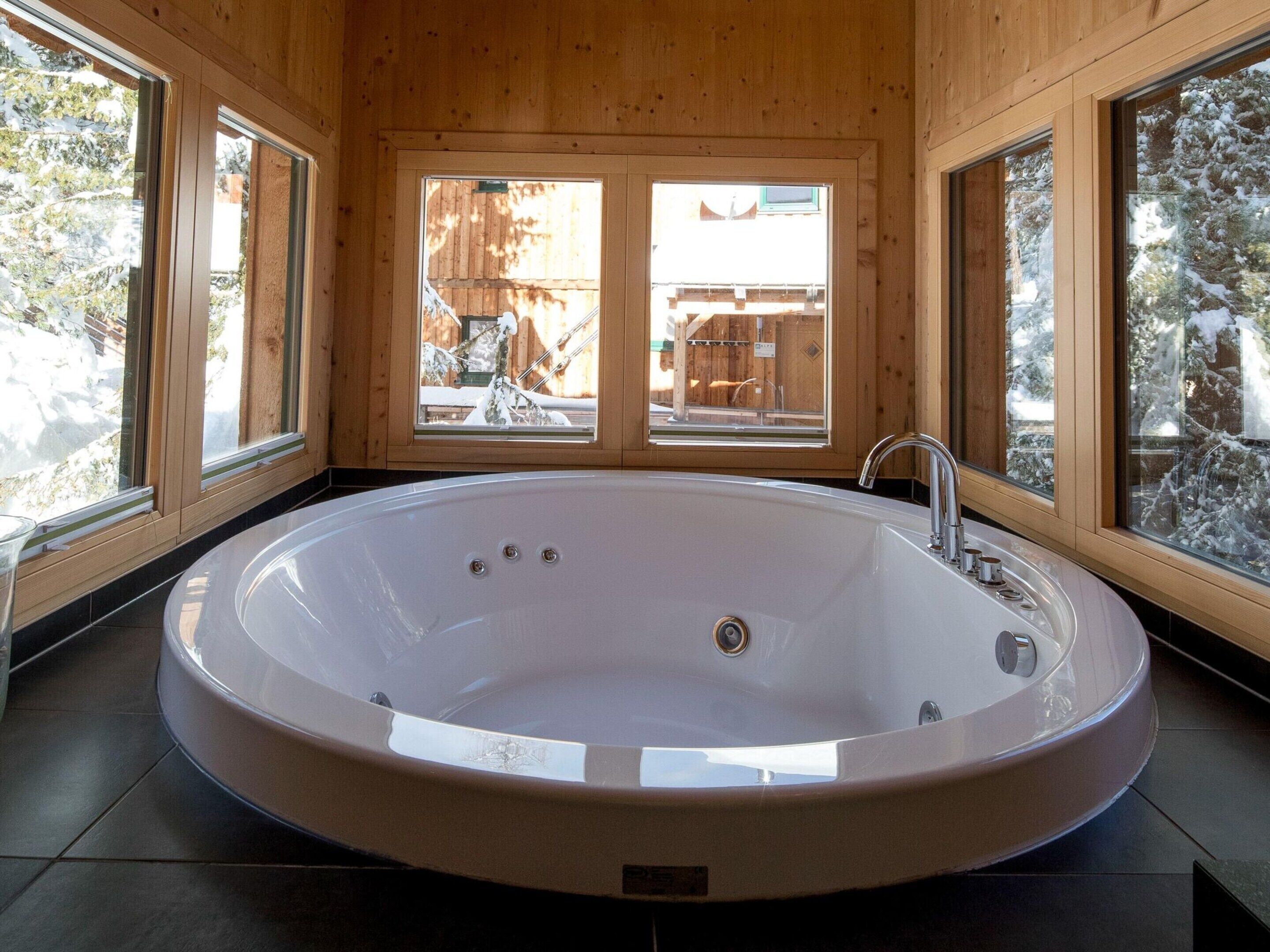 A large, oval-shaped bathtub in a wooden cabin with large windows.