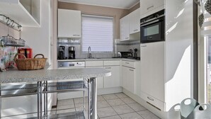 Een moderne keuken met witte kasten, een ingebouwde oven, een koffiezetapparaat en een raam met zonwering.