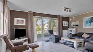 Een woonkamer met een bank, fauteuil, televisie en een schuifdeur naar buiten.