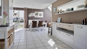 A modern kitchen with white cabinetry, a dining area with a table and chairs, and a view through a large window. - Bungalow in Breskens Near Lighthouse & Beach (Breskens)