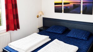 A bedroom with a bed, a nightstand, a lamp, and a window with red curtains. - Holiday Home Breskens Near Scenic Beaches (Breskens)