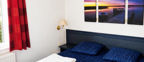 A bedroom with a bed, a nightstand, a lamp, and a window with red curtains.