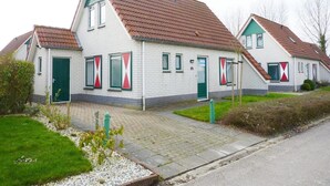 A row of white houses with red and green window shutters, a paved driveway, and a grassy area with a small garden. - Holiday Home Breskens Near Scenic Beaches (Breskens)