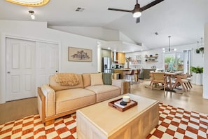 Un salón espacioso con un sofá color beige, una mesa de centro de madera y un tapete de cuadros.