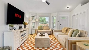 A living room with a checkered floor, a flat-screen TV, a ceiling fan, and a large window. - Stunning 3BR Home-Backyard HOT TUB Oasis-Home Gym (Boise)