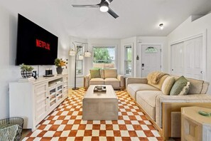 A living room with a checkered floor, a flat-screen TV, a ceiling fan, and a large window.